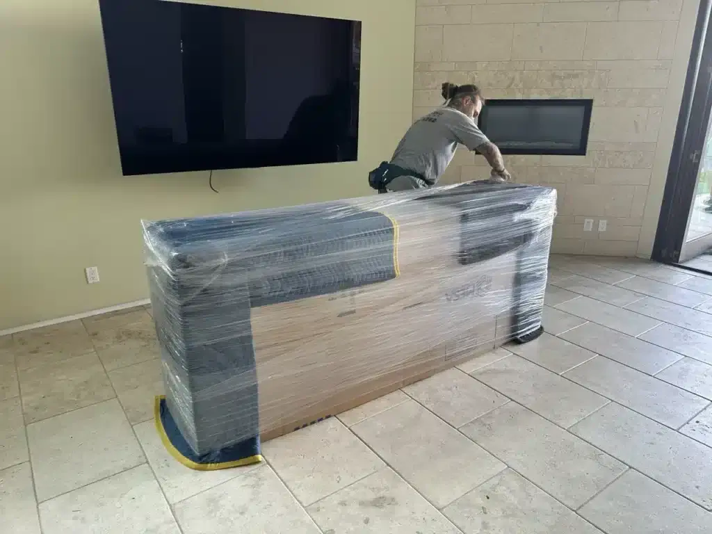 Professional movers wrapping a credenza with moving blankets and stretch wrap to protect furniture during a residential move.