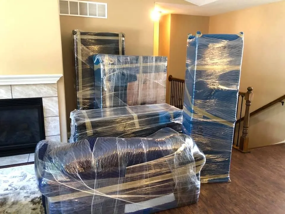 Professional movers wrapping furniture with moving blankets and stretch wrap before a residential move.